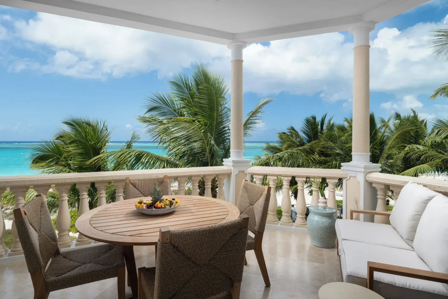 Oceanfront balcony with round dining table, lounge seating, and palms at Point Grace.