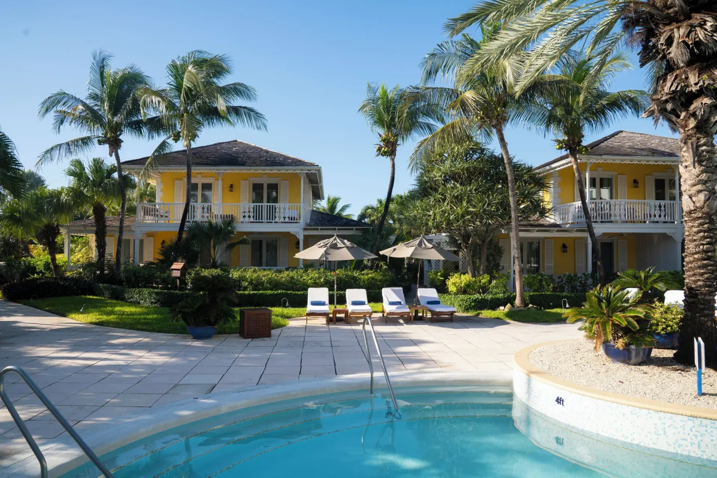 Pool edge with loungers, palms, and yellow guest buildings at Point Grace.