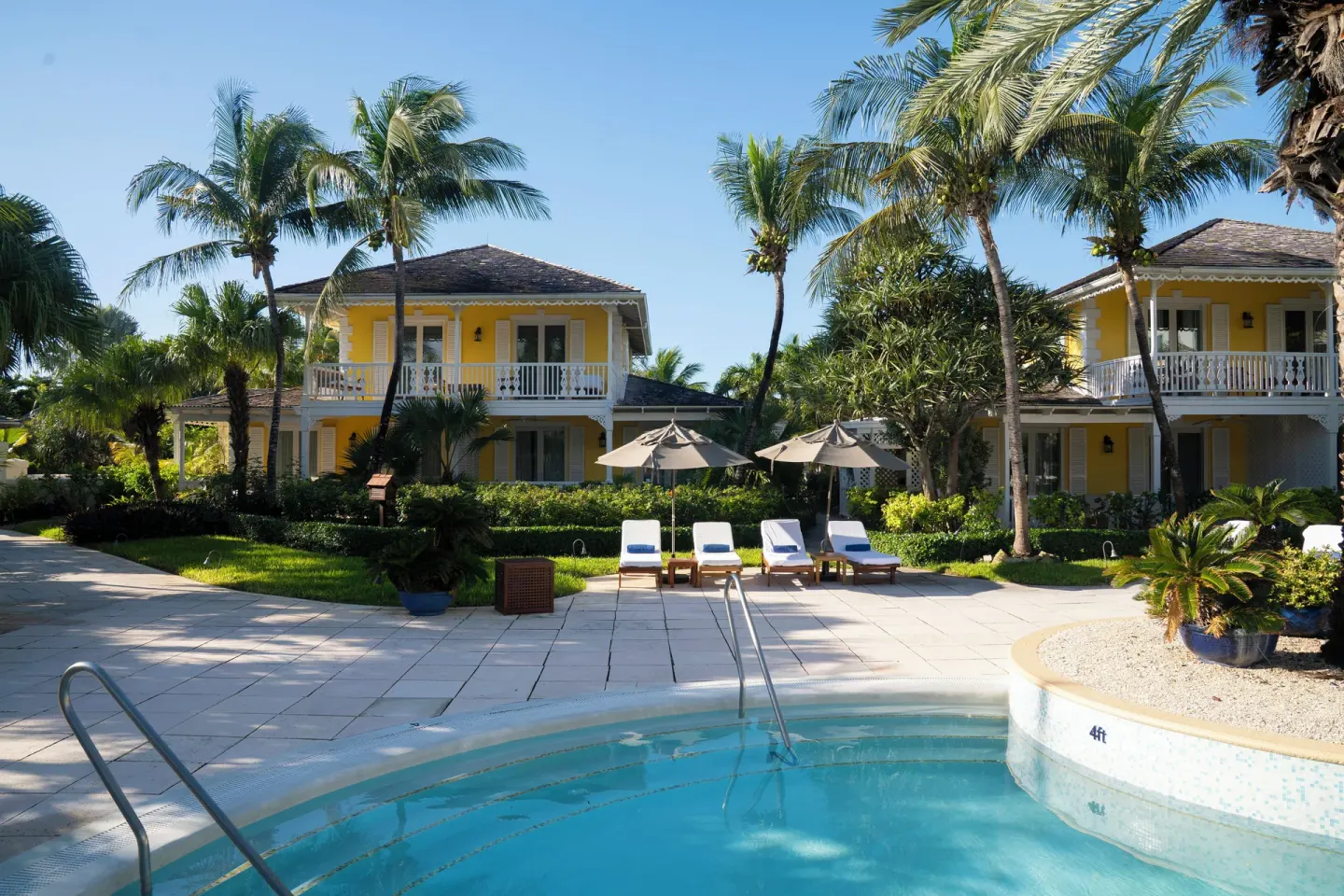 Poolside view of yellow resort buildings, palms, loungers, and umbrellas at Point Grace.