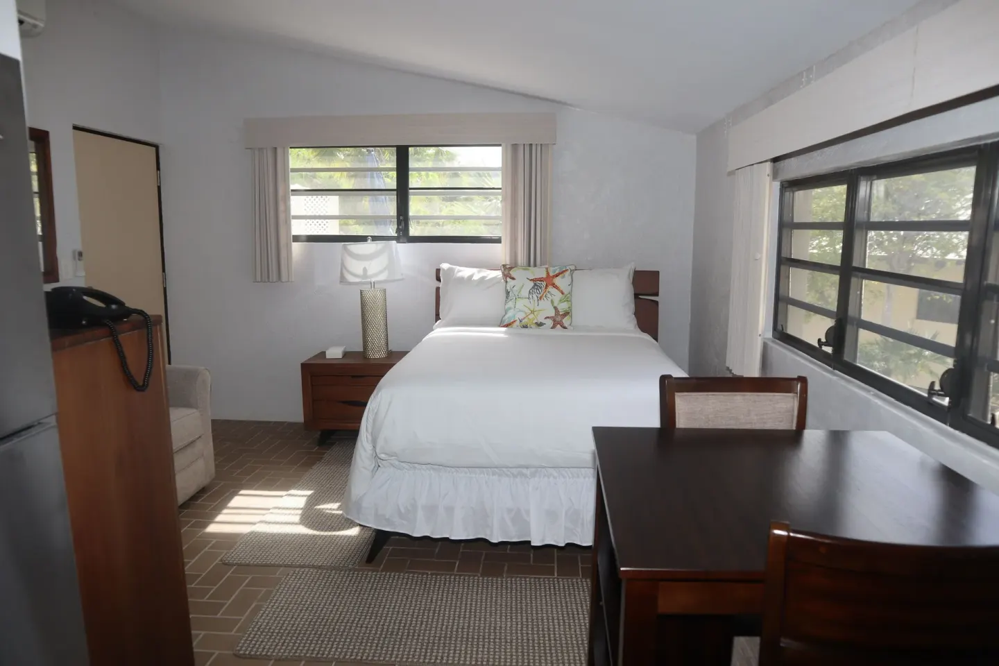 Compact guest room with queen bed, dining table and windows at Point Pleasant Resort.
