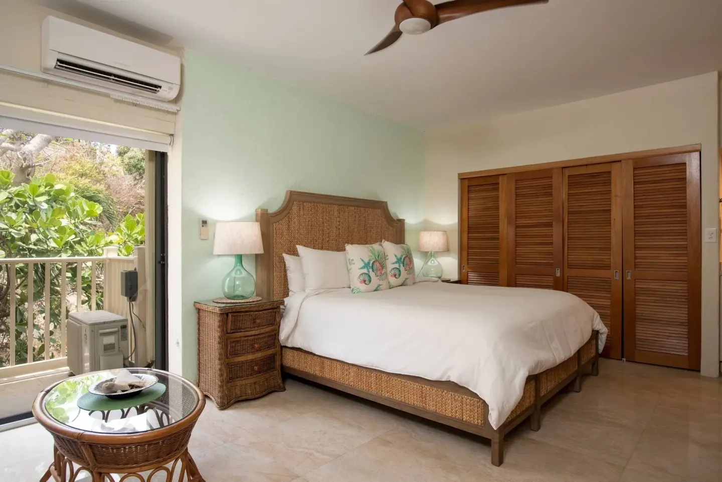 Guest room with bed, wicker table, balcony doors, and closet at Point Pleasant Resort.
