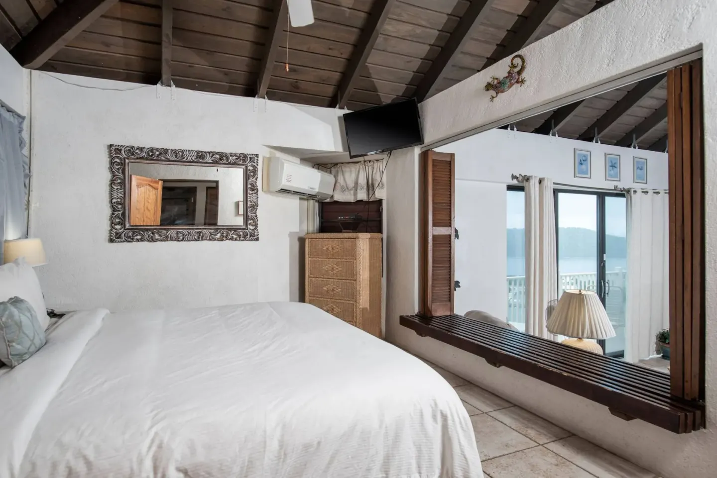 Guest room bed with an interior window framing balcony doors at Point Pleasant Resort.
