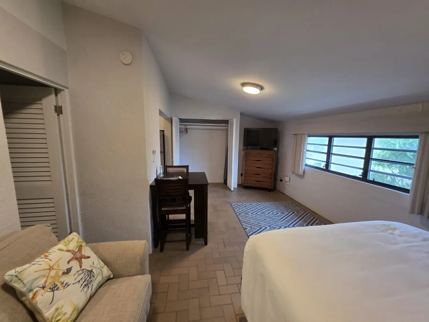 Guest room with bed, sofa, desk, closet, dresser, and windows at Point Pleasant Resort.