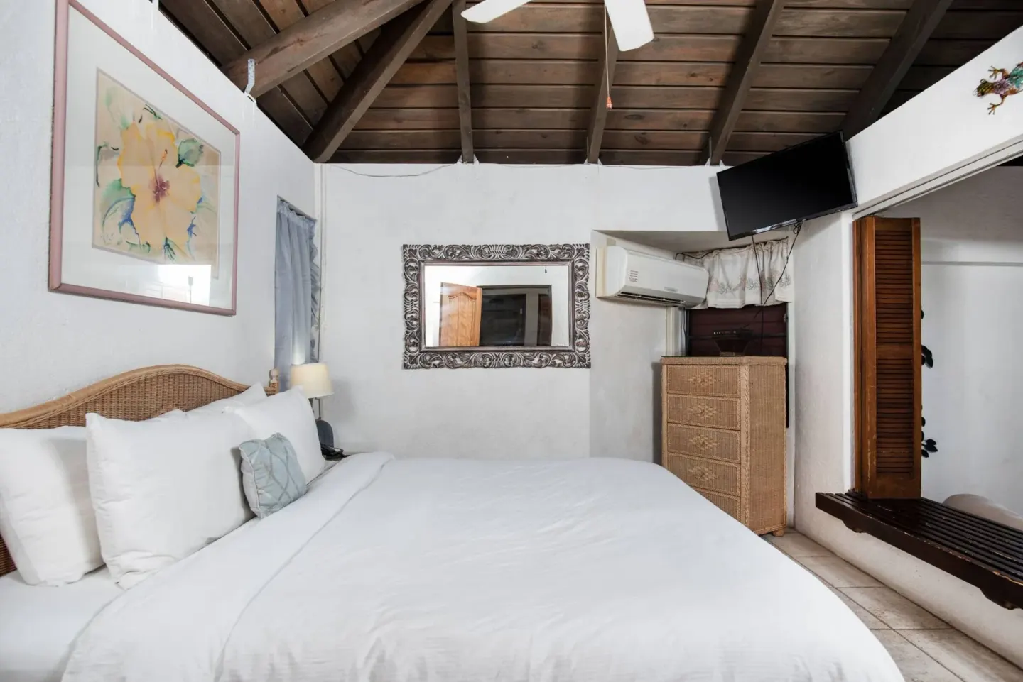 Guest room with a white bed, wicker dresser, mirror, and wood ceiling at Point Pleasant Resort.