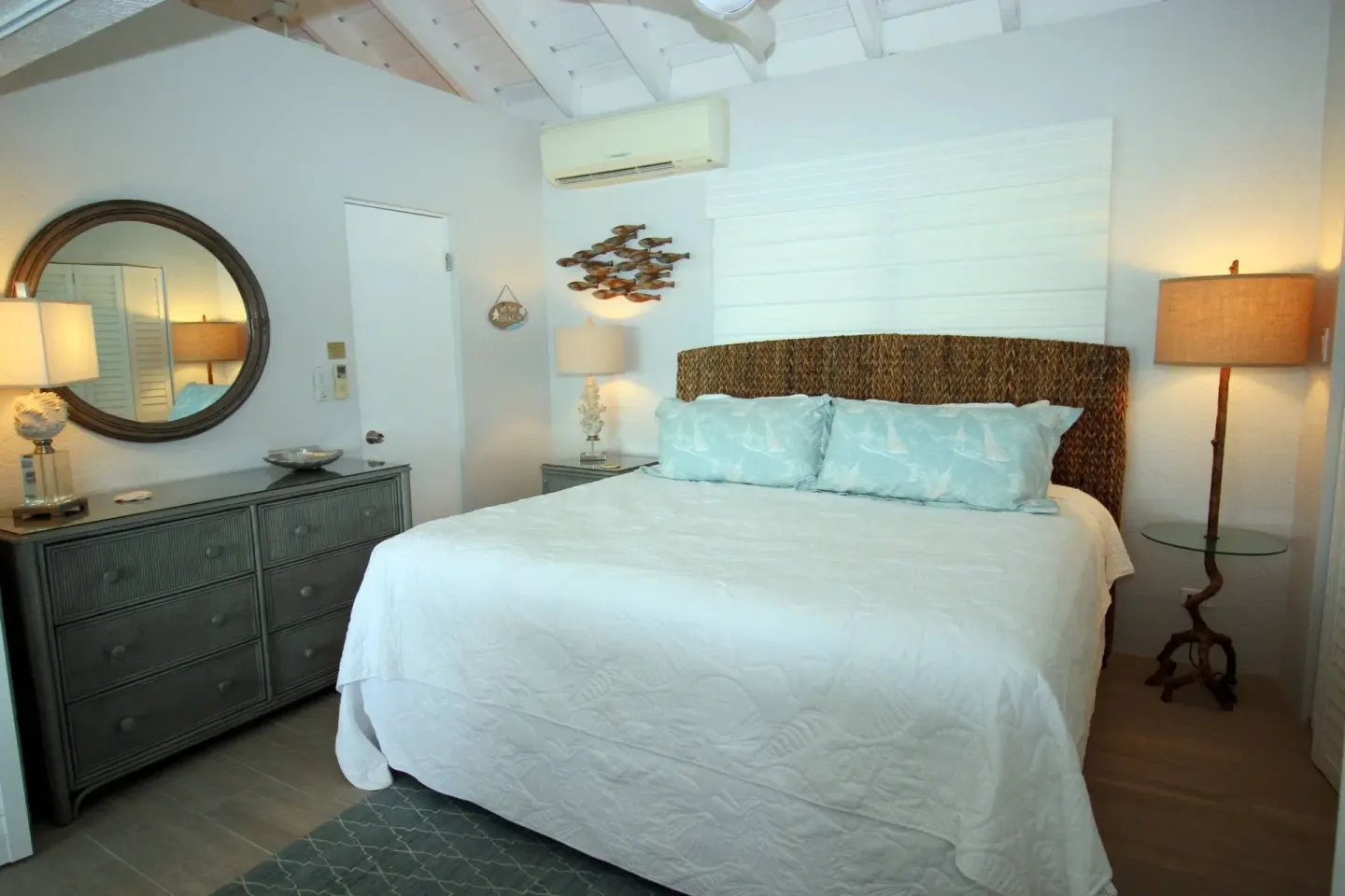 Guest room with white bed, woven headboard, dresser, and lamps at Point Pleasant Resort.