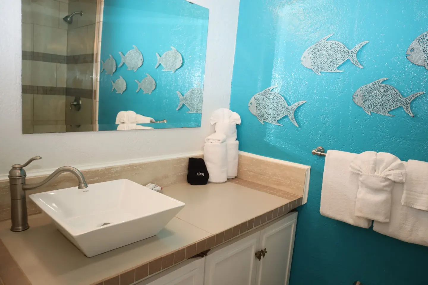 Studio bathroom vanity with vessel sink, mirror, towels, and fish wall decor at Point Pleasant Resort.
