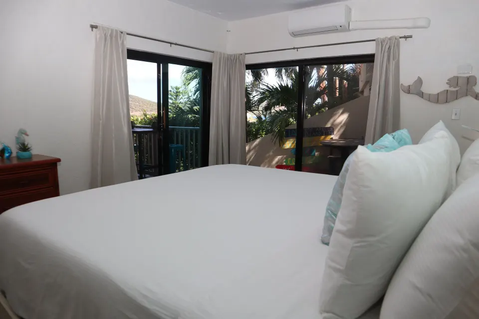 Studio bed beside sliding glass doors and curtained windows at Point Pleasant Resort.