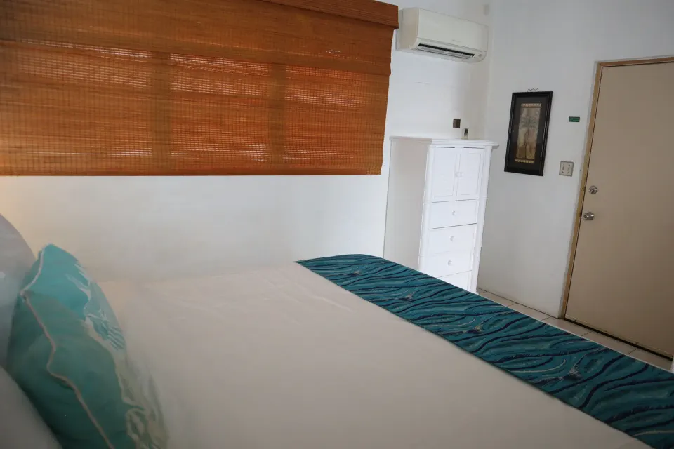Studio king bed beside woven shade, dresser, and wall air unit at Point Pleasant Resort.