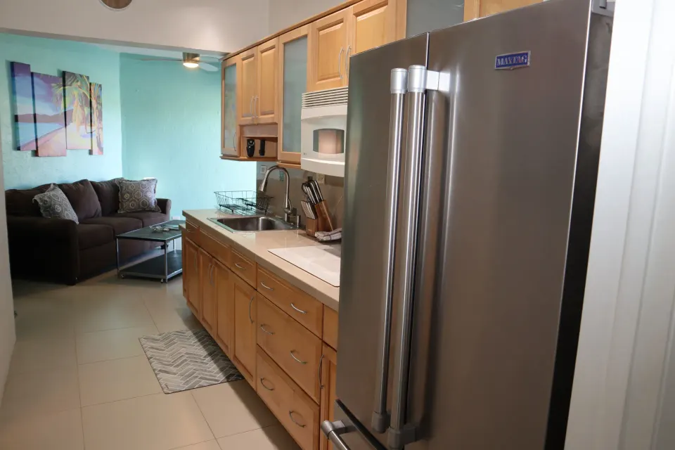 Studio kitchen with stainless refrigerator, wood cabinets, sink, microwave, and sofa beyond at Point Pleasant Resort.
