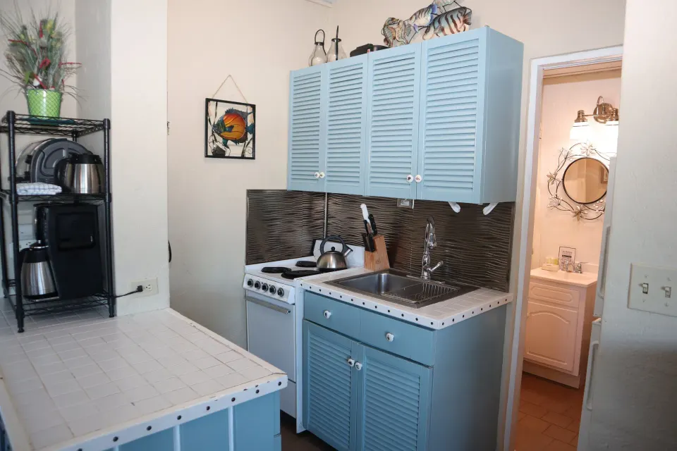 Studio kitchenette with blue cabinets, sink, cooktop, and bathroom doorway at Point Pleasant Resort.