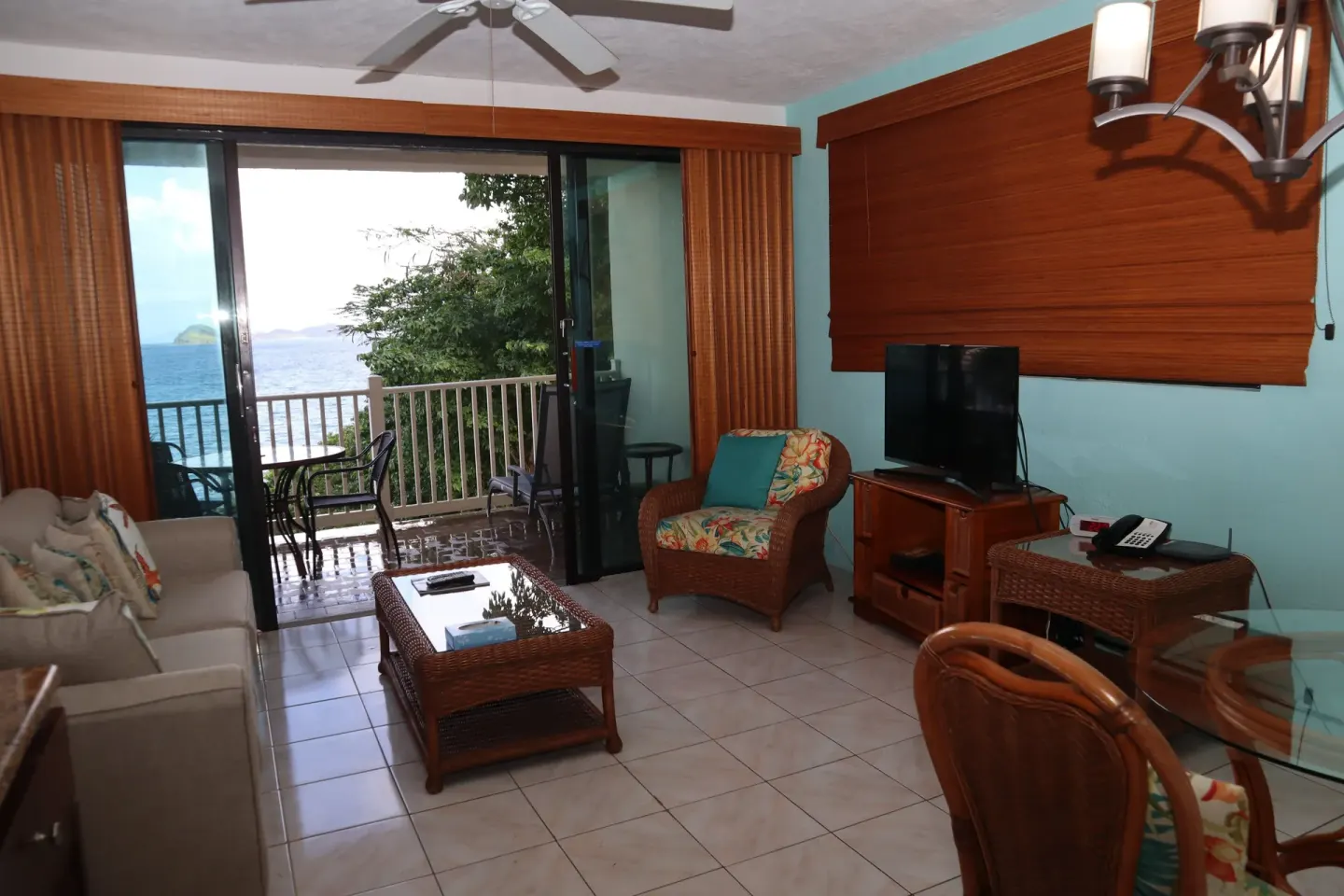 Studio living room with sofa, TV, wicker chair, and balcony at Point Pleasant Resort.