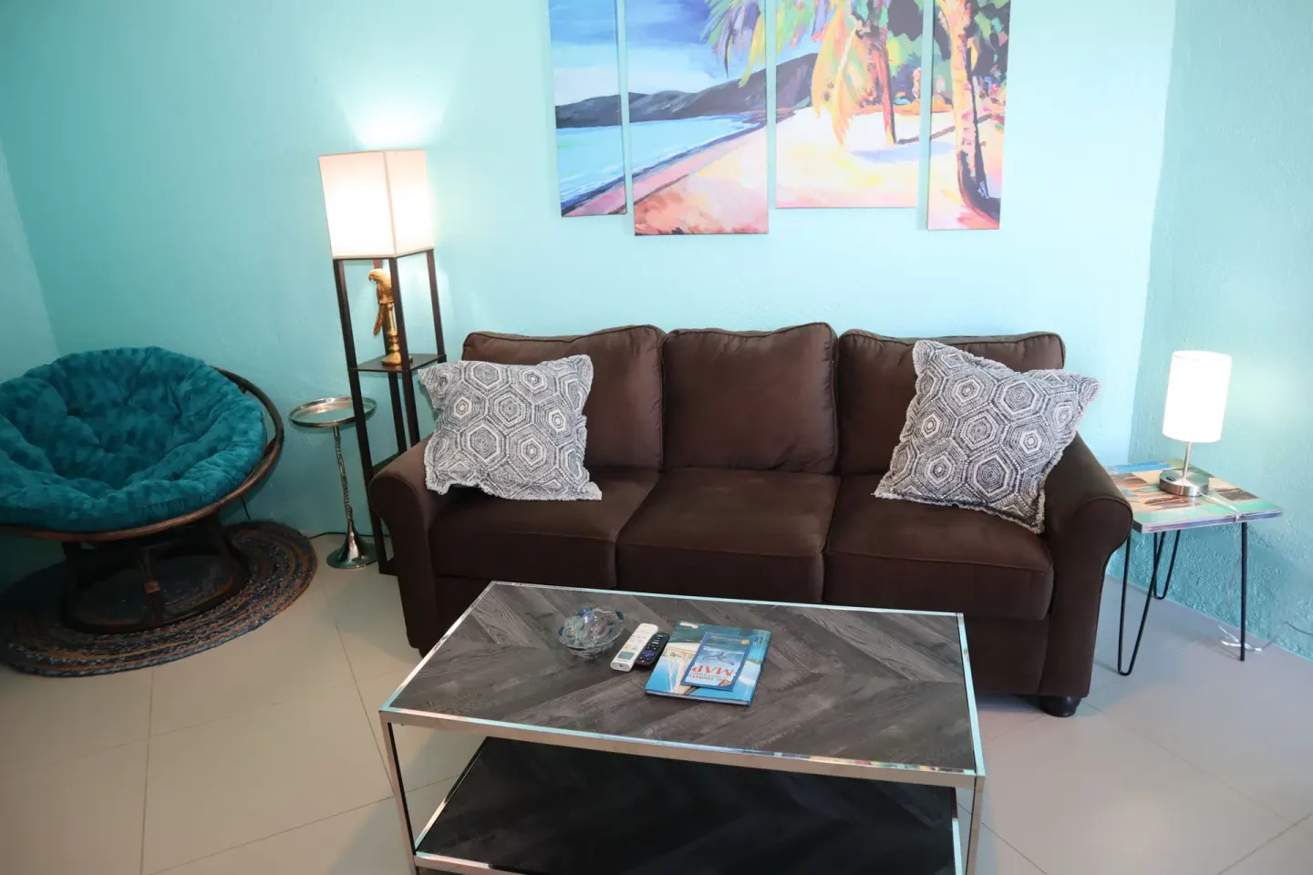 Studio lounge with sofa, papasan chair, tables, and tropical wall art at Point Pleasant Resort.