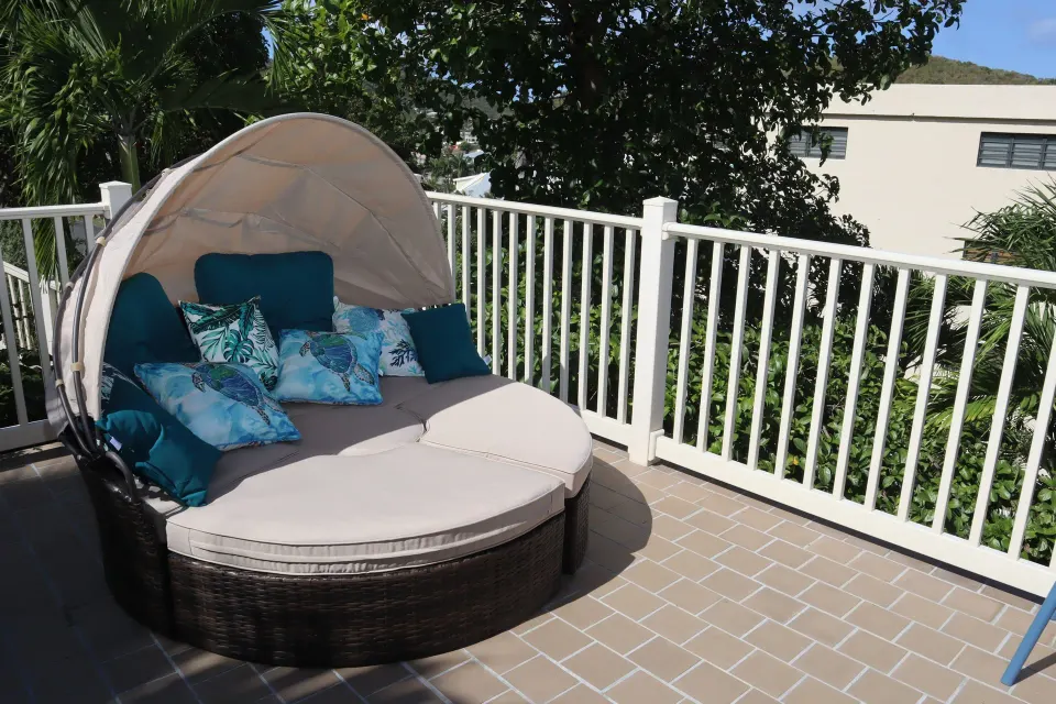 Studio terrace daybed with canopy, cushions, white railing, and leafy surroundings at Point Pleasant Resort.