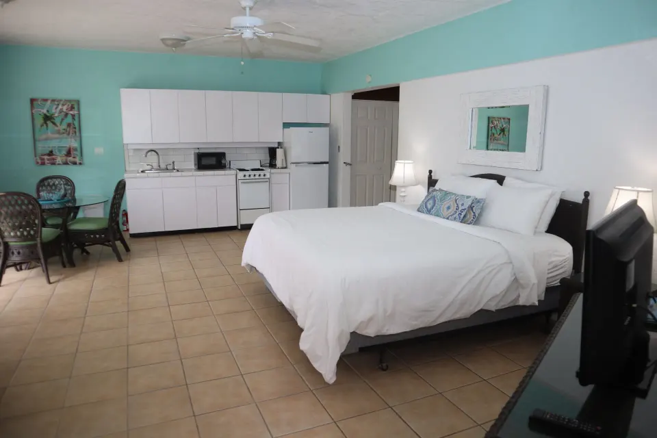 Studio with white bed, kitchenette, dining nook, and TV at Point Pleasant Resort.