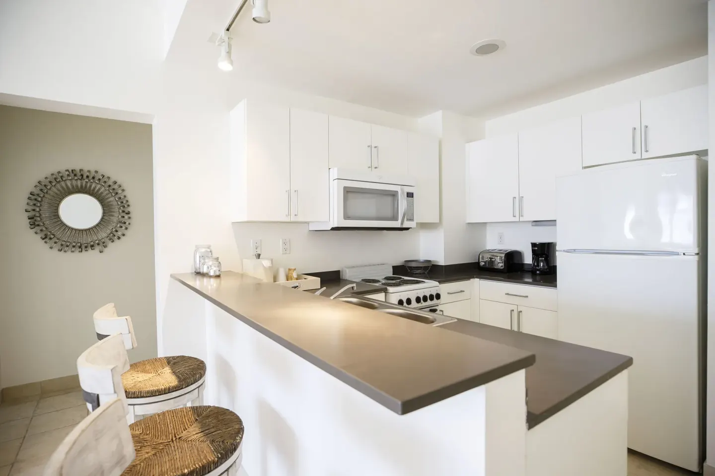 Compact white kitchenette with breakfast bar and stools at Ports of Call Resort.