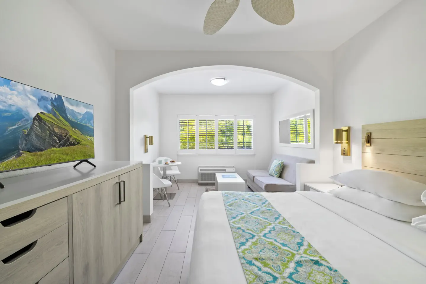 Guest room with king bed, sofa, TV, and shuttered windows at Ports of Call Resort.