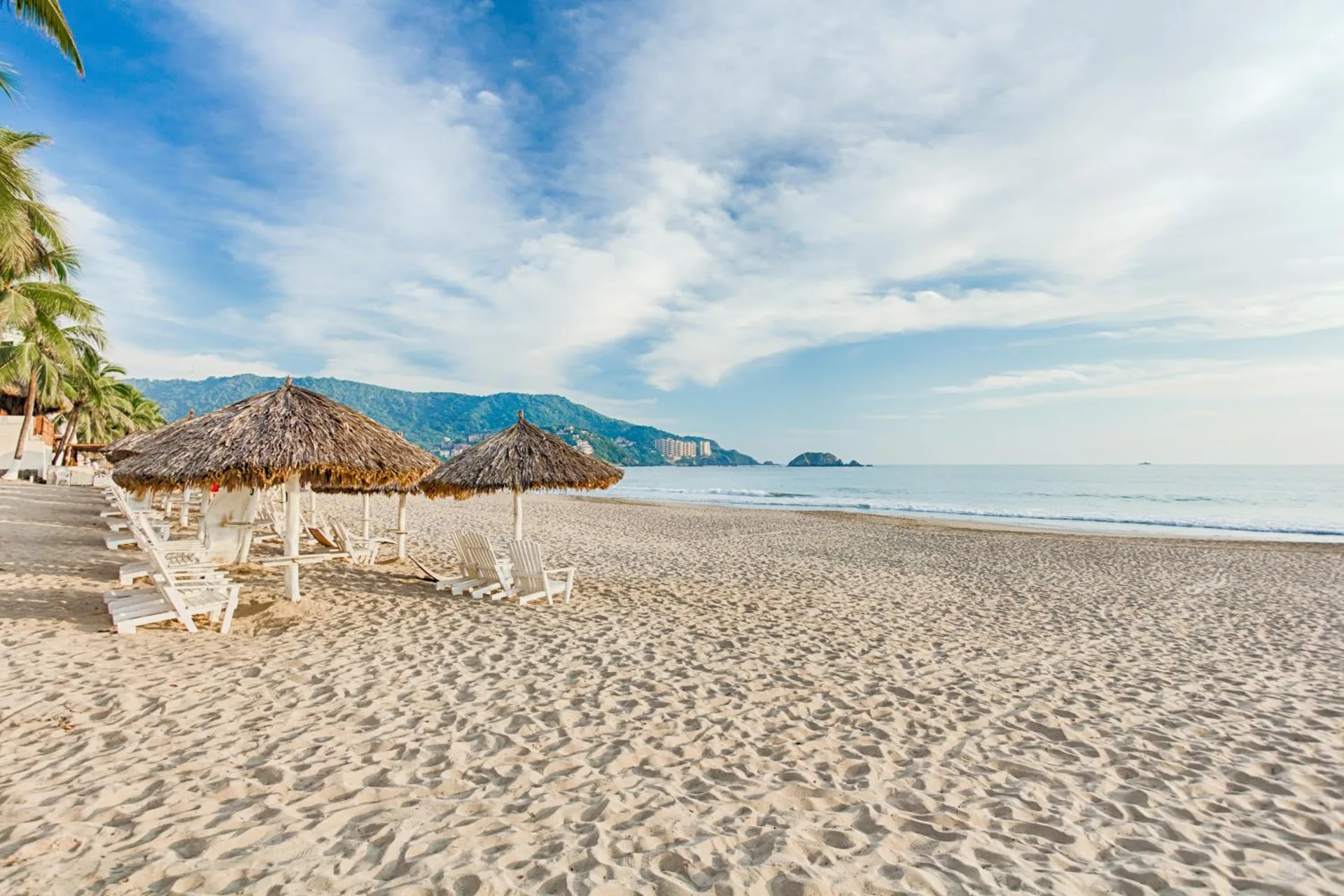 Sandy beach with palapas, loungers, and calm surf at Posada Real Ixtapa.