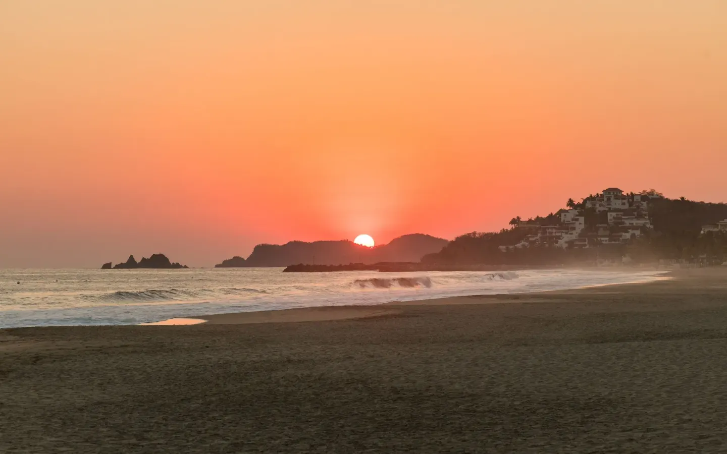 Sunset over the beach with waves and distant hills at Posada Real Ixtapa.