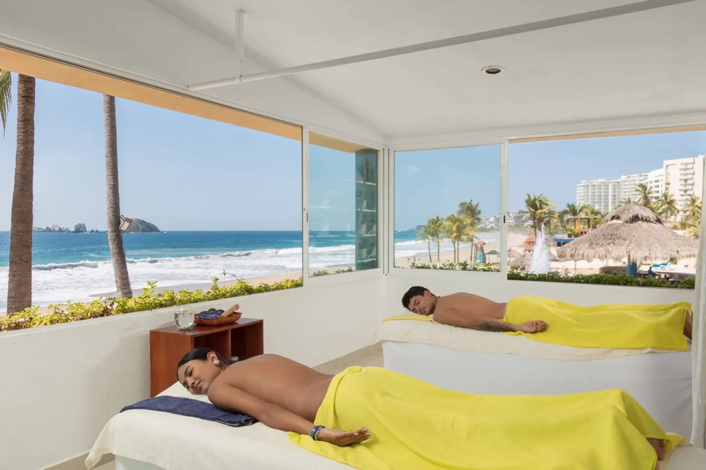Two guests relax on massage tables beside beach-facing windows at Posada Real Ixtapa.
