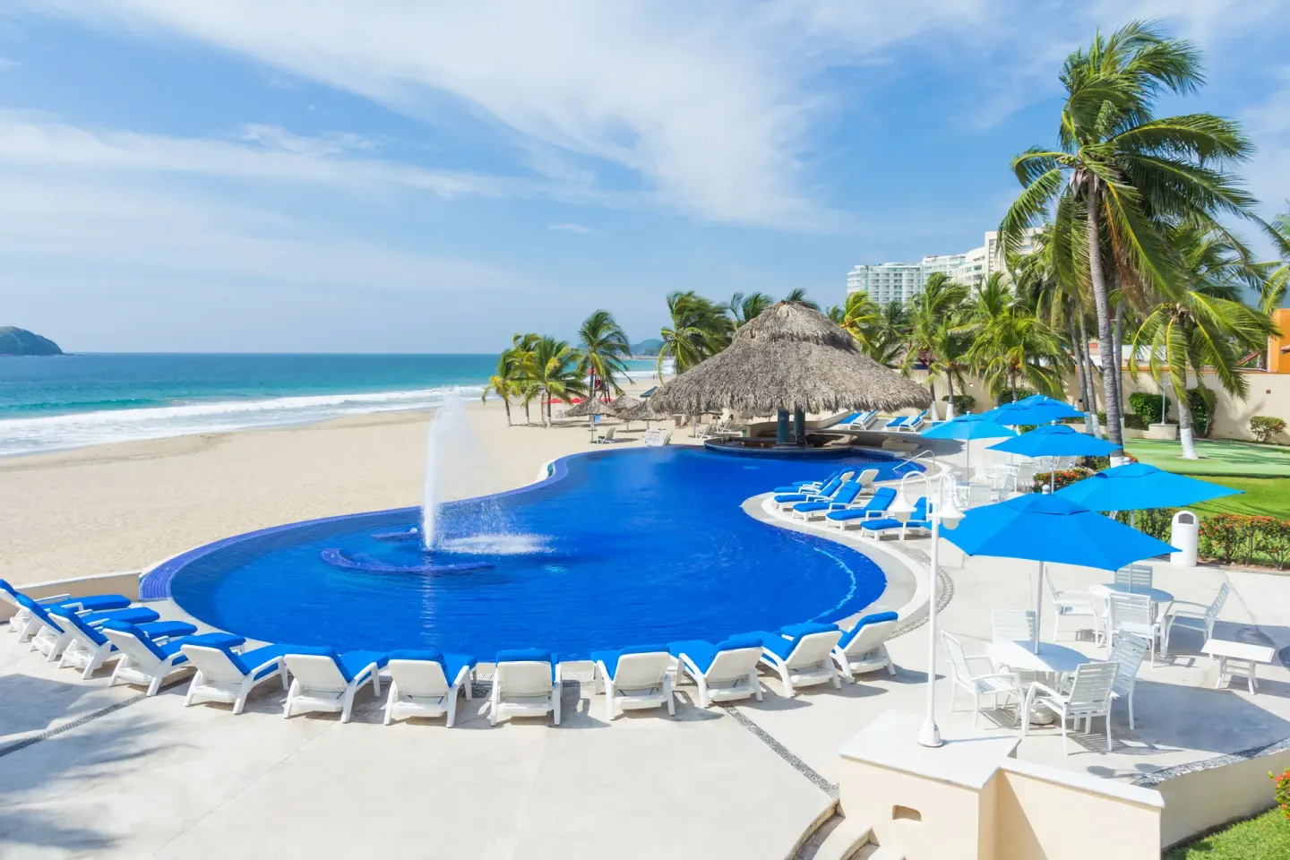 Beachfront pool deck with blue loungers and umbrellas at Posada Real Ixtapa.
