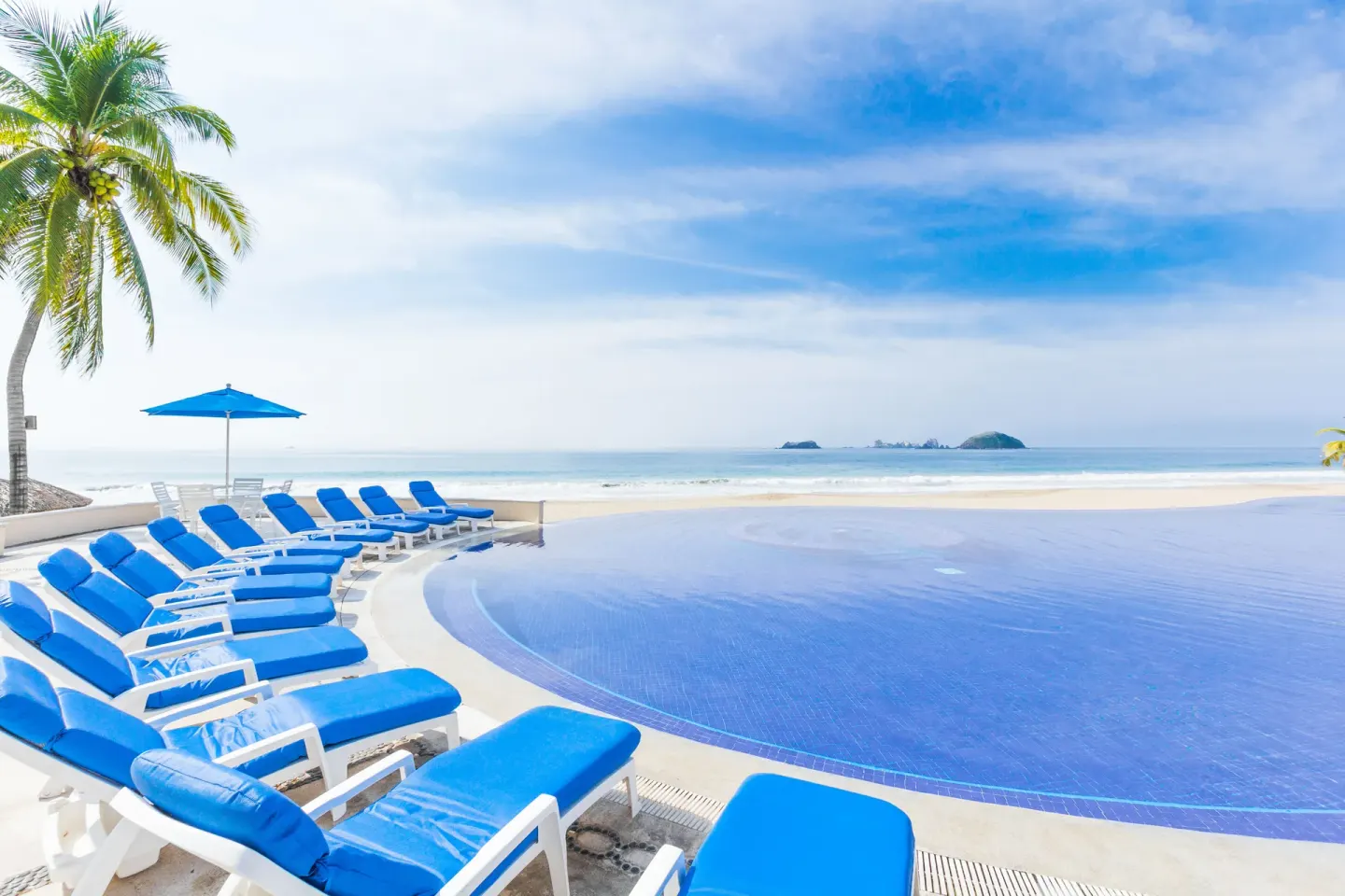 Curved pool edge and blue loungers face the beach at Posada Real Ixtapa.