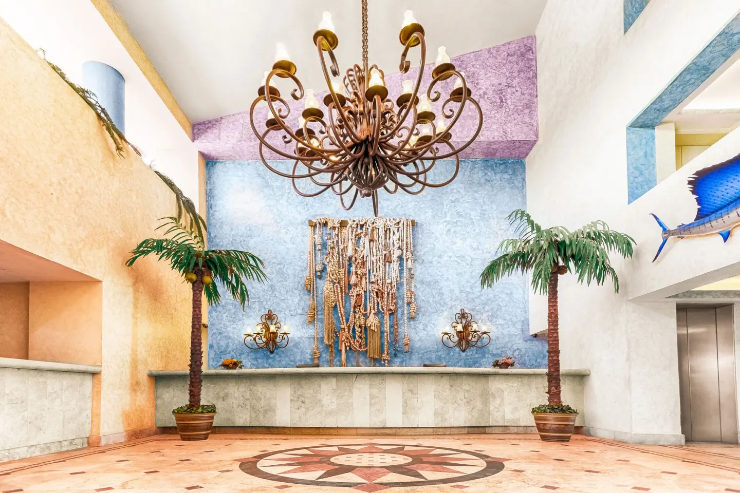Colorful lobby with chandelier, palms, and nautical wall decor at Posada Real Ixtapa.