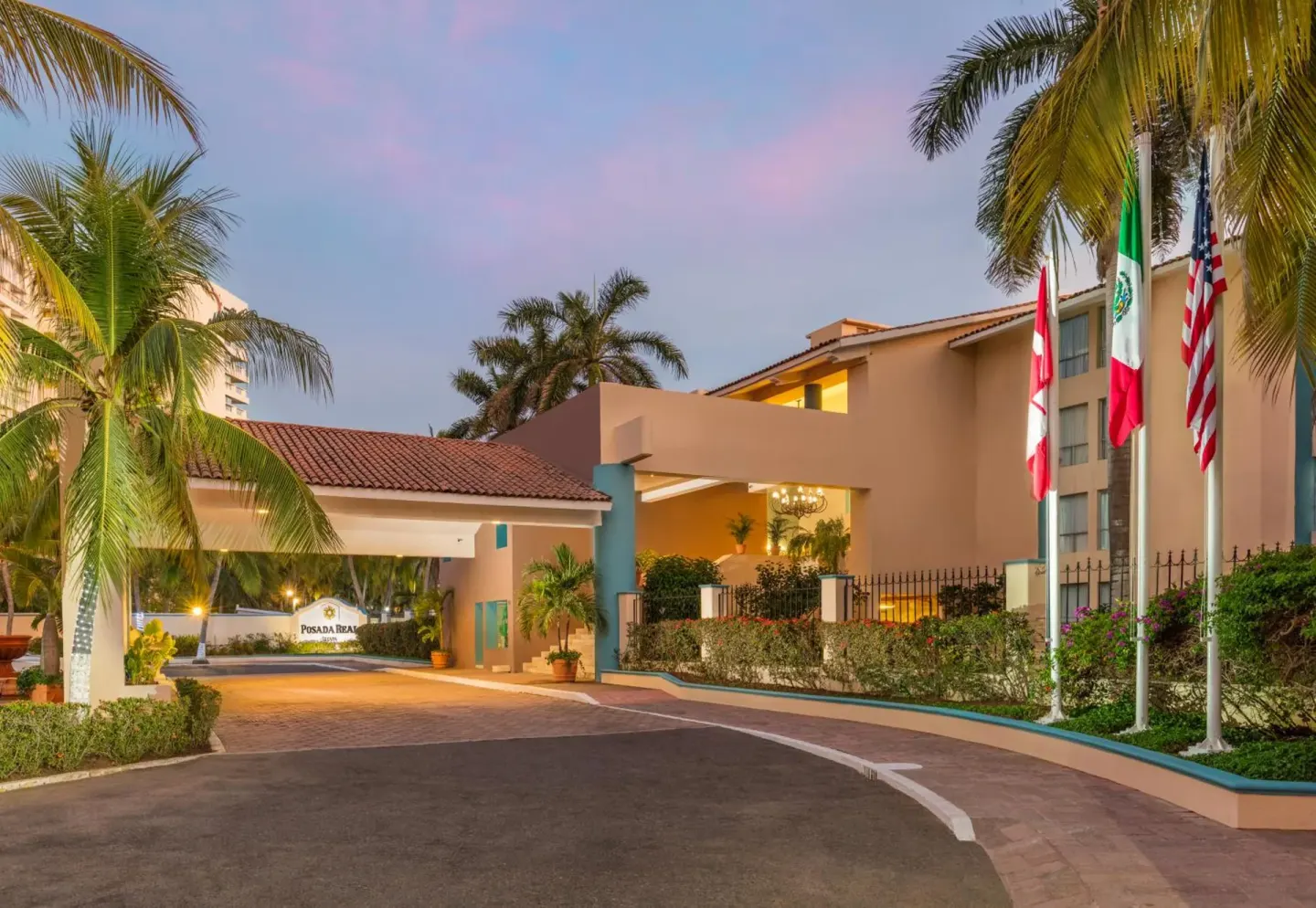 Evening entrance driveway with flags and palms at Posada Real Ixtapa.
