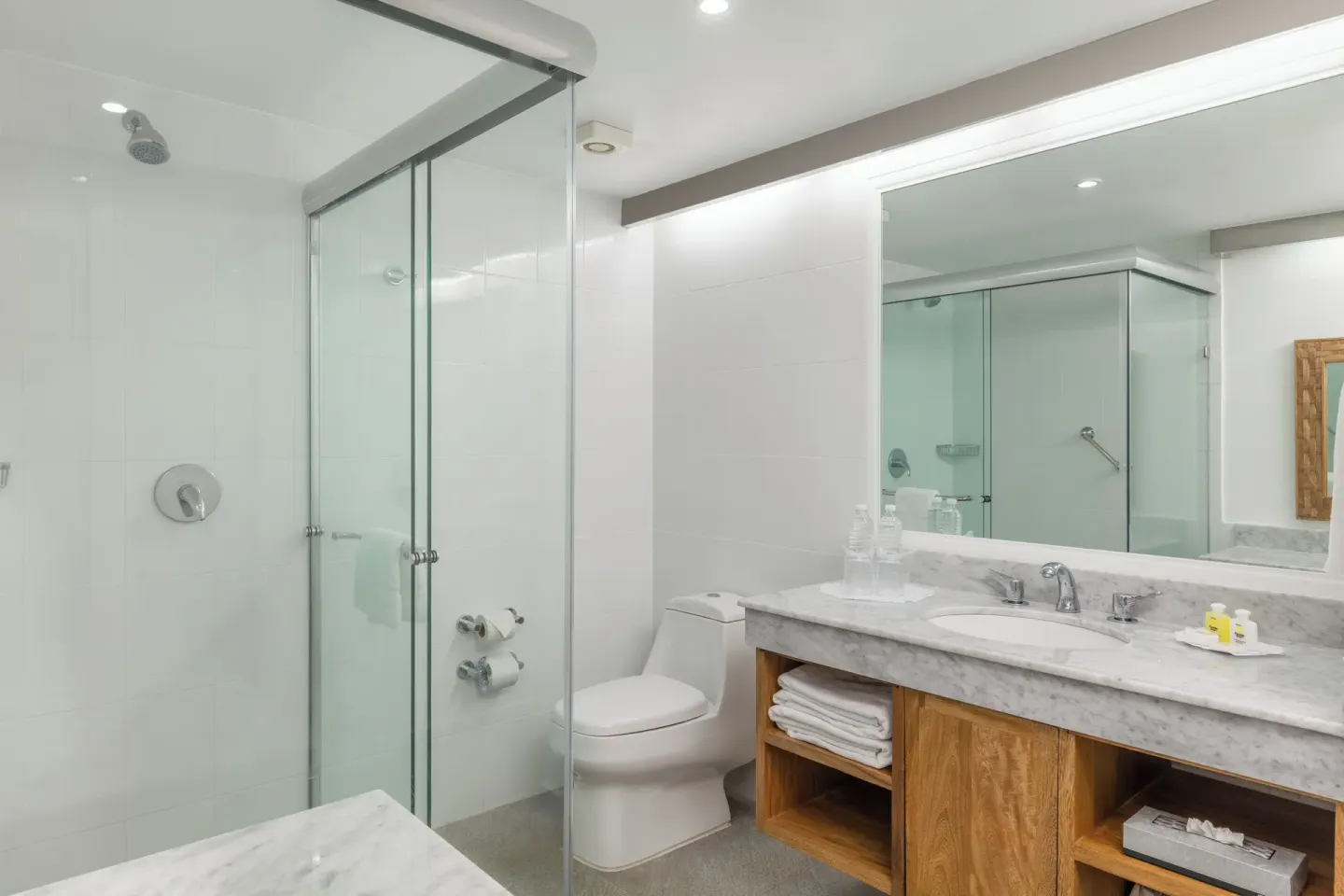 Bathroom with glass shower, toilet, vanity, towels, and amenities at Posada Real Ixtapa.