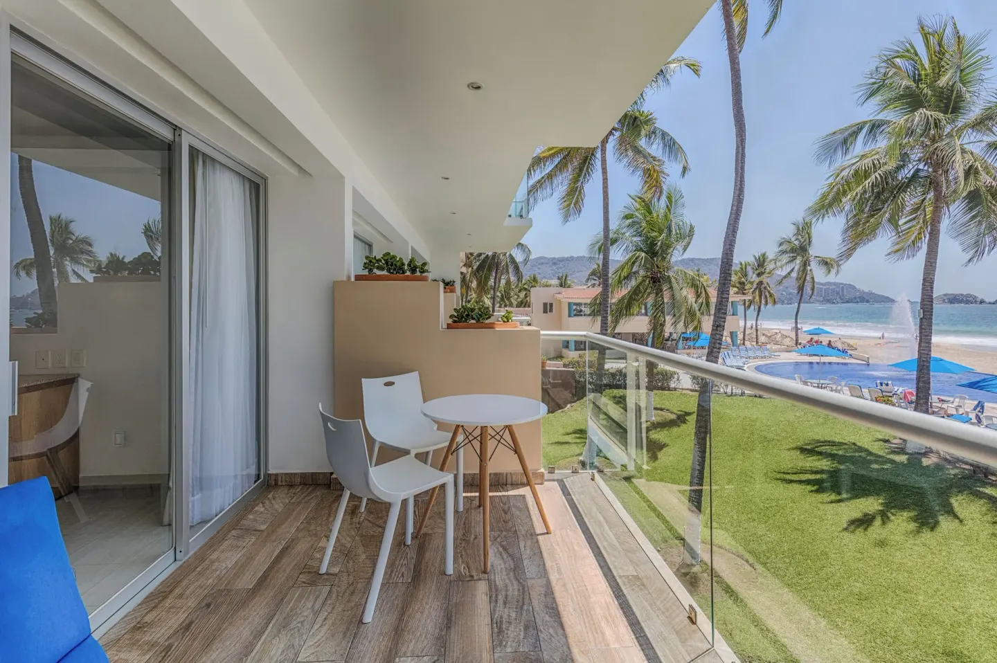 Balcony with table and chairs overlooking palms, lawn, pool, and beach at Posada Real Ixtapa.