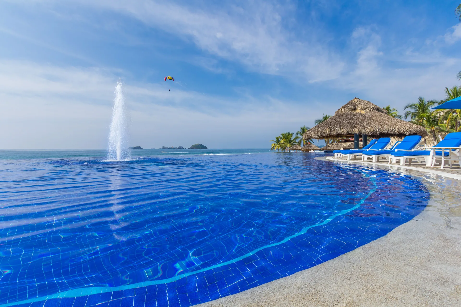Oceanfront pool with fountain, palapa shade and blue loungers at Posada Real Ixtapa.