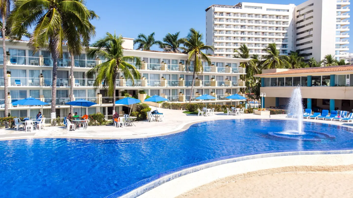 A blue pool, fountain, palms, and resort buildings at Posada Real Ixtapa.