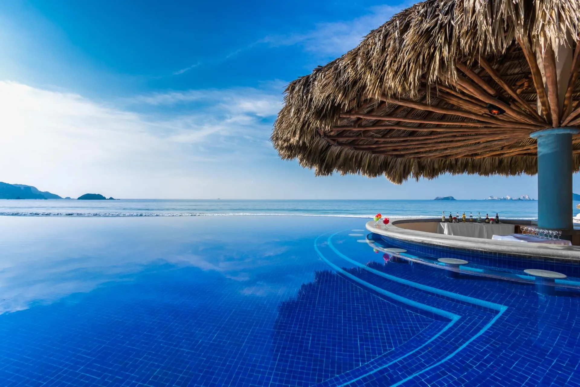 Swim-up pool bar with thatched roof facing the ocean at Posada Real Ixtapa.