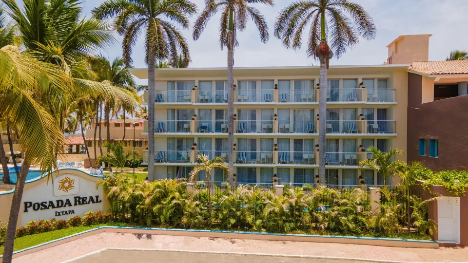 Exterior guest room balconies and Posada Real Ixtapa sign among palm trees.