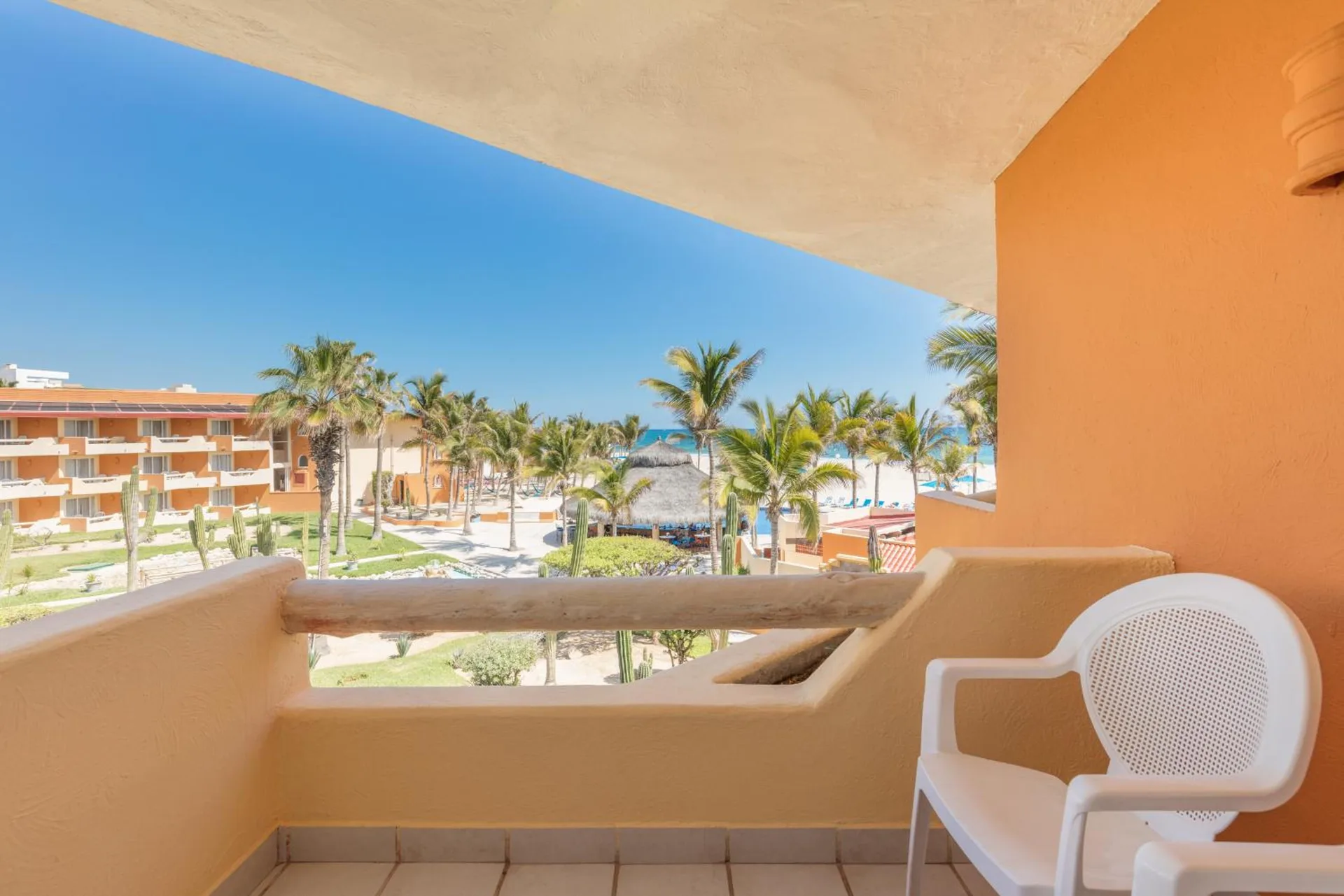 A balcony at Posada Real Los Cabos overlooks palms, gardens, the pool area, and the ocean beyond.
