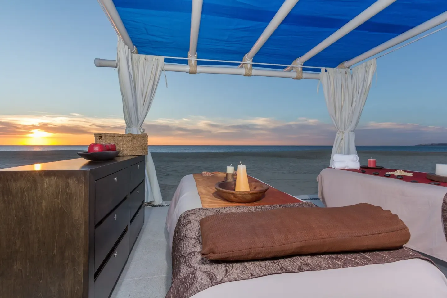 Beach massage table under a blue canopy at sunset at Posada Real Los Cabos.