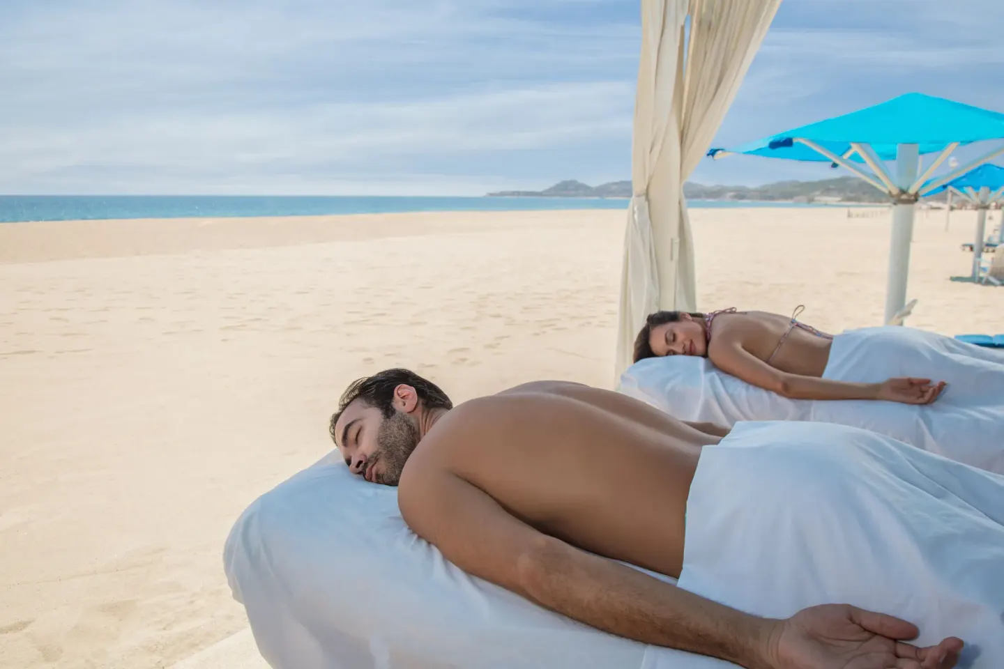 Two guests resting on beach massage tables at Posada Real Los Cabos.