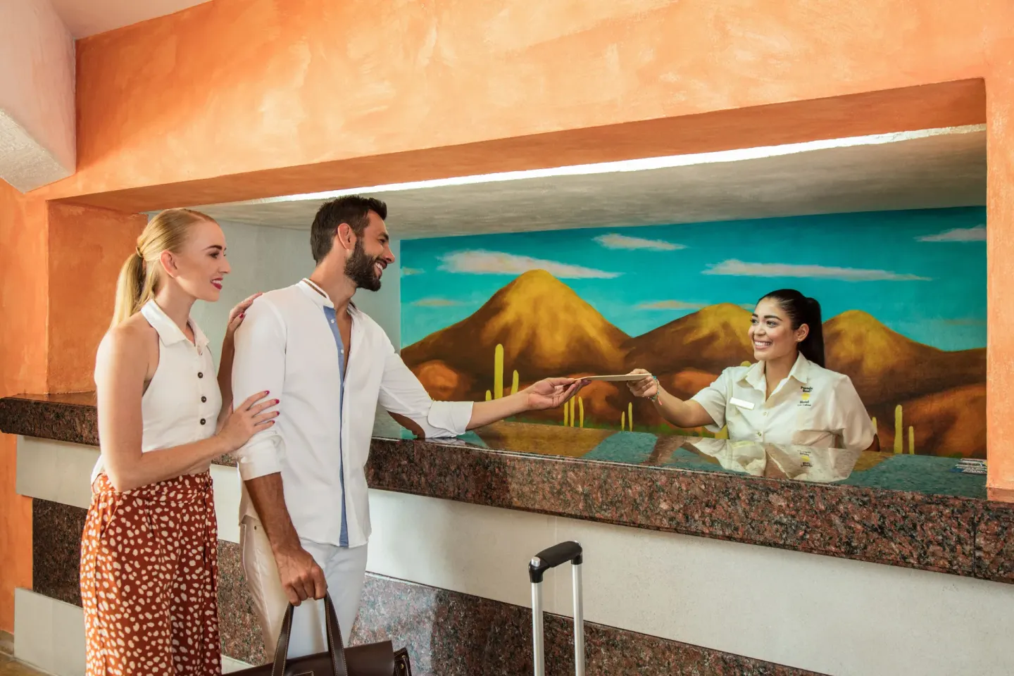 Guests checking in at the front desk with a desert mural at Posada Real Los Cabos.