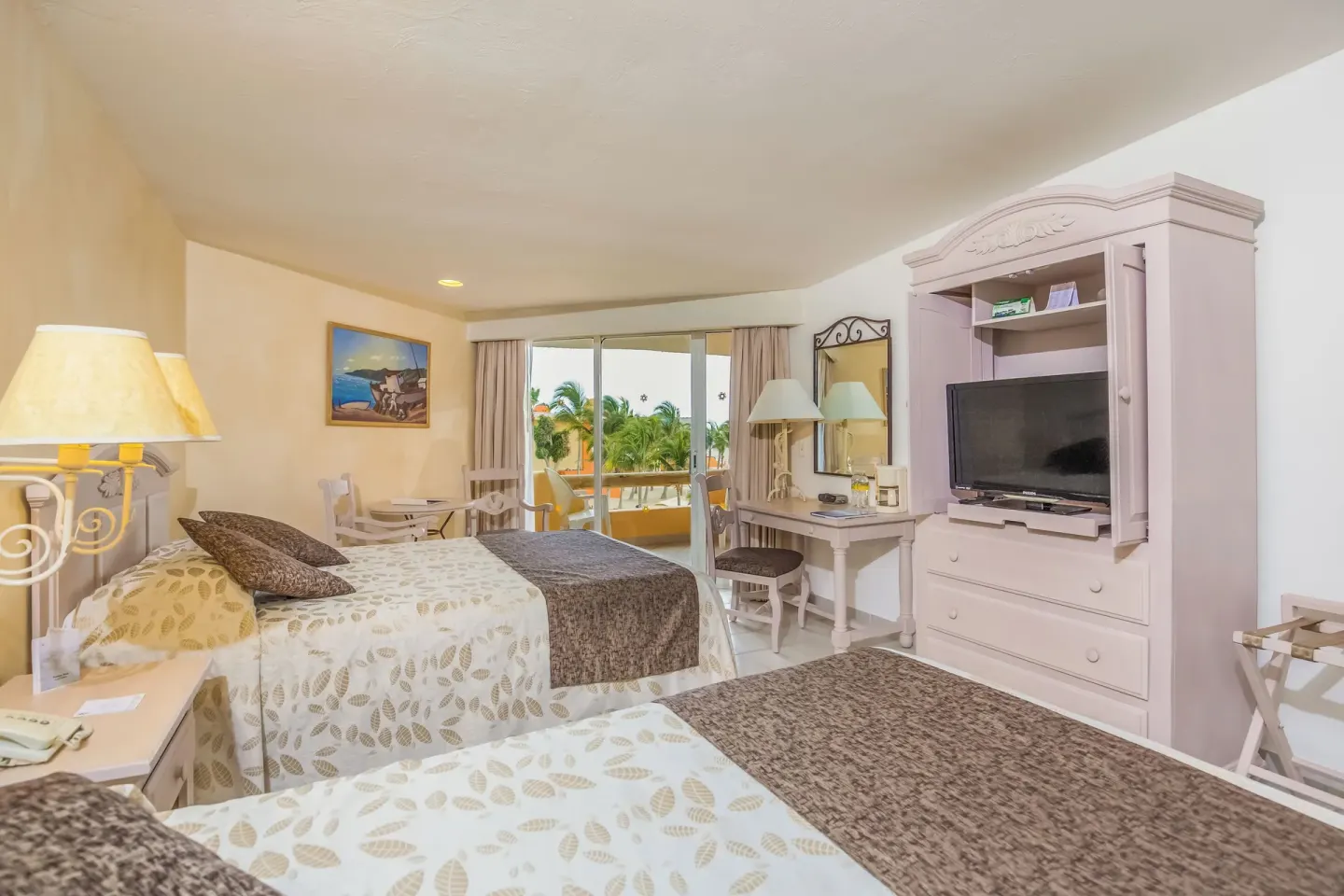 Guest room with two beds, TV cabinet, desk, and balcony at Posada Real Los Cabos.