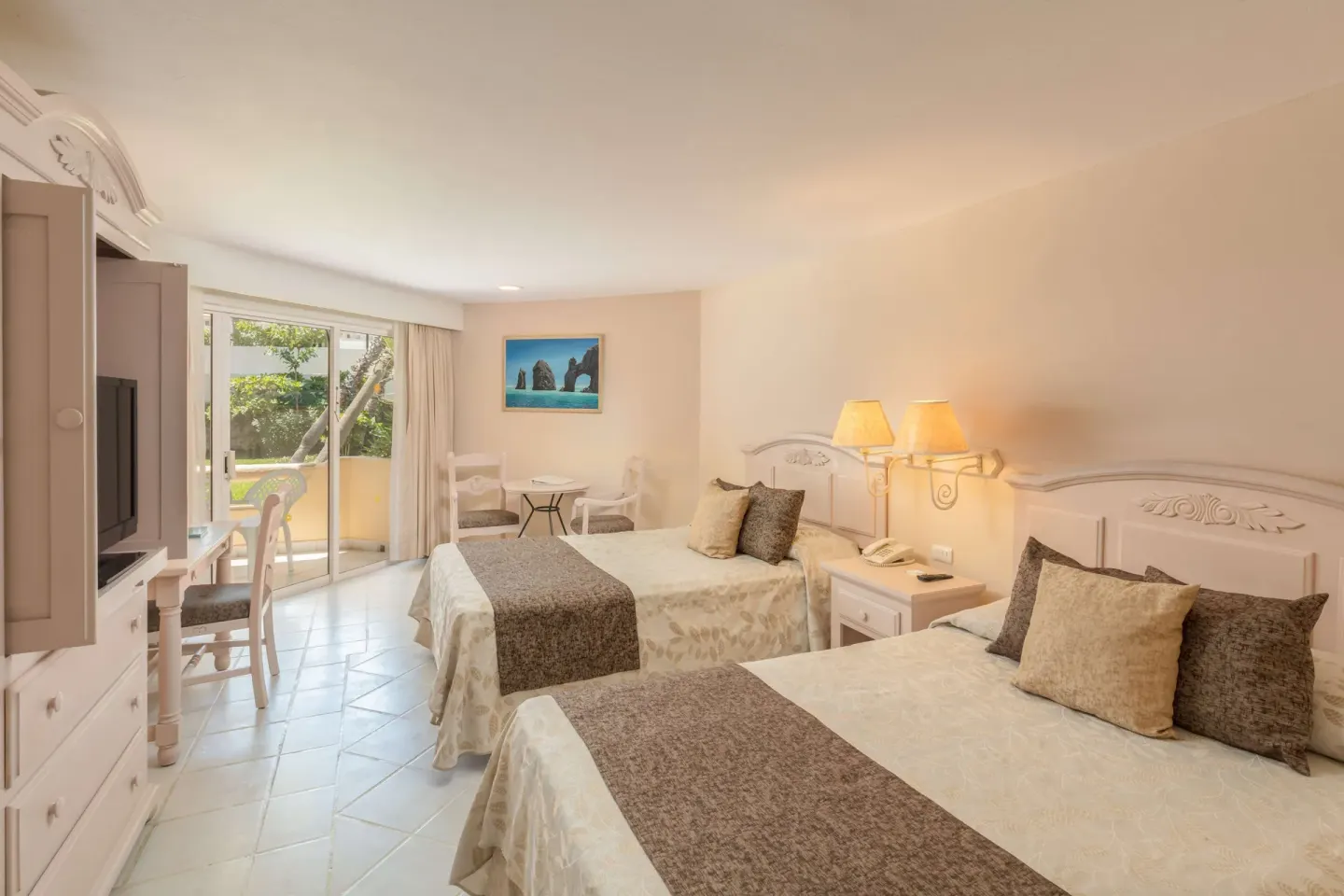 Guest room with two beds, seating area, and balcony doors at Posada Real Los Cabos.