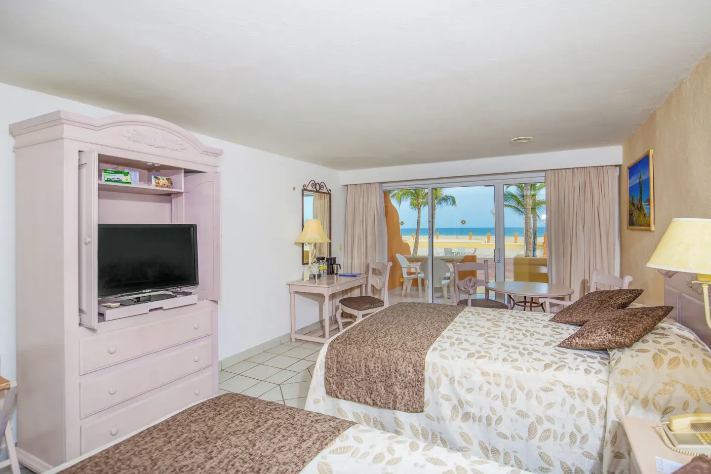 Guest room with two beds, TV cabinet, and ocean-facing balcony at Posada Real Los Cabos.