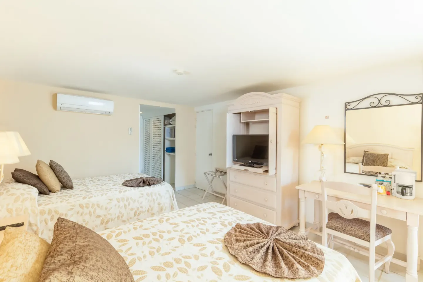 Guest room with two beds, dresser, vanity, and open closet at Posada Real Los Cabos.