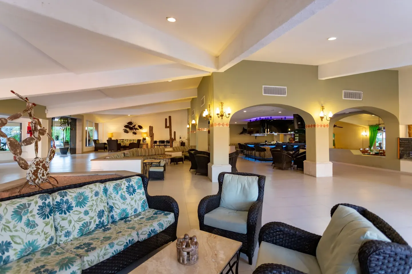 Lobby seating area with wicker chairs, floral sofa and arched bar at Posada Real Los Cabos.