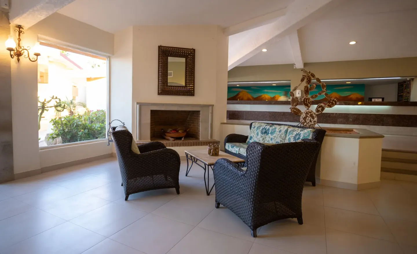 Lobby sitting area with wicker furniture, fireplace and window at Posada Real Los Cabos.