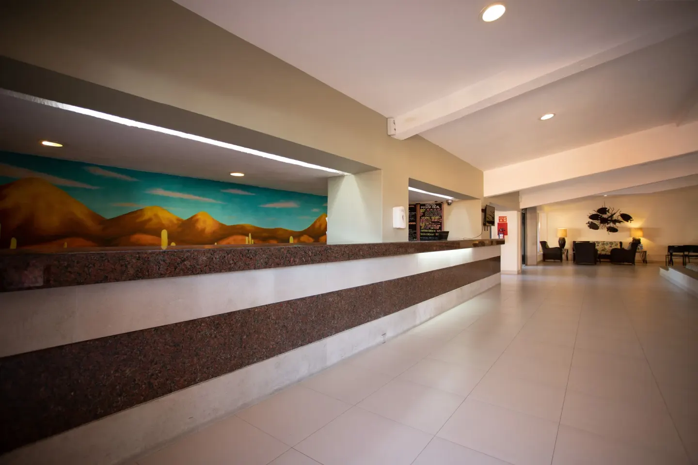 Long reception counter with a desert mural and lobby seating at Posada Real Los Cabos.