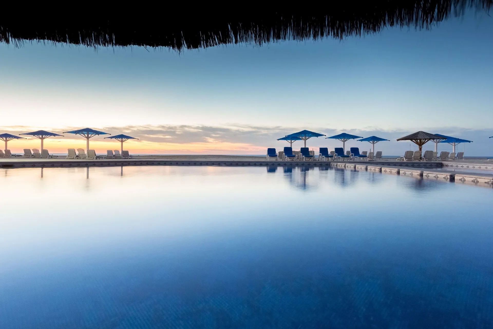 Pool at sunrise with lounge chairs and blue umbrellas at Posada Real Los Cabos.