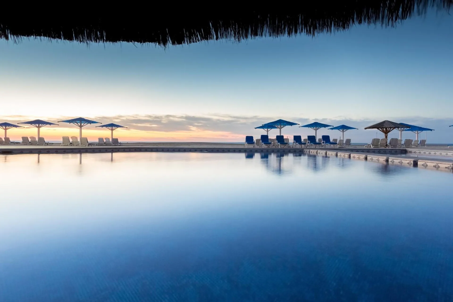 Sunset pool scene with loungers and blue umbrellas at Posada Real Los Cabos.