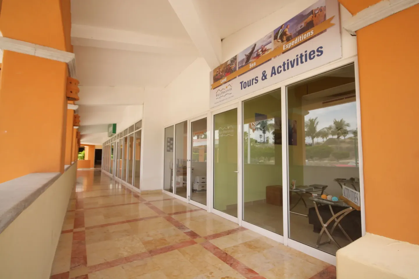 A covered corridor at Posada Real Los Cabos shows glass doors and a Tours & Activities sign.