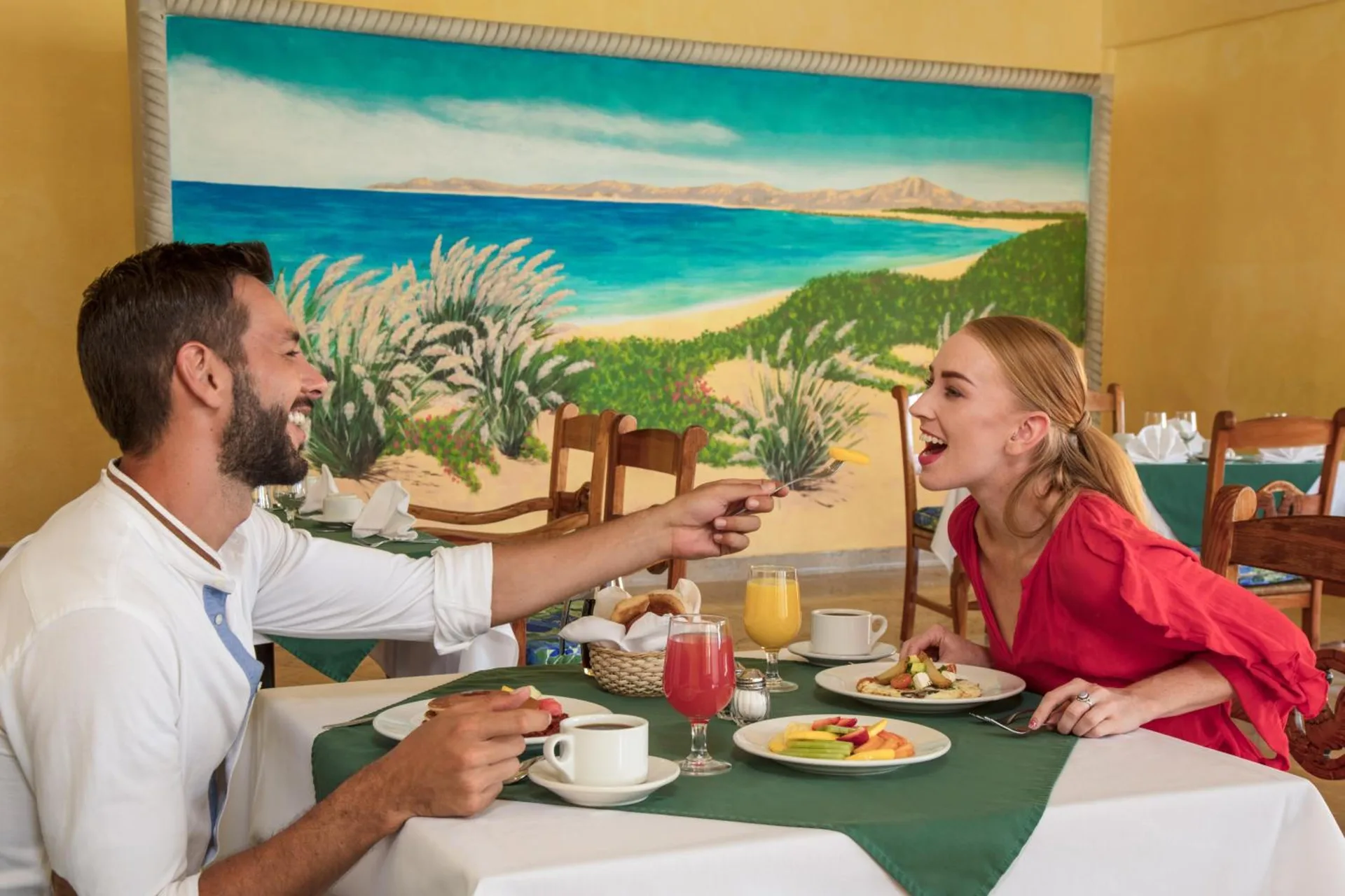 Couple dining at a table beneath a coastal mural at Posada Real Los Cabos.