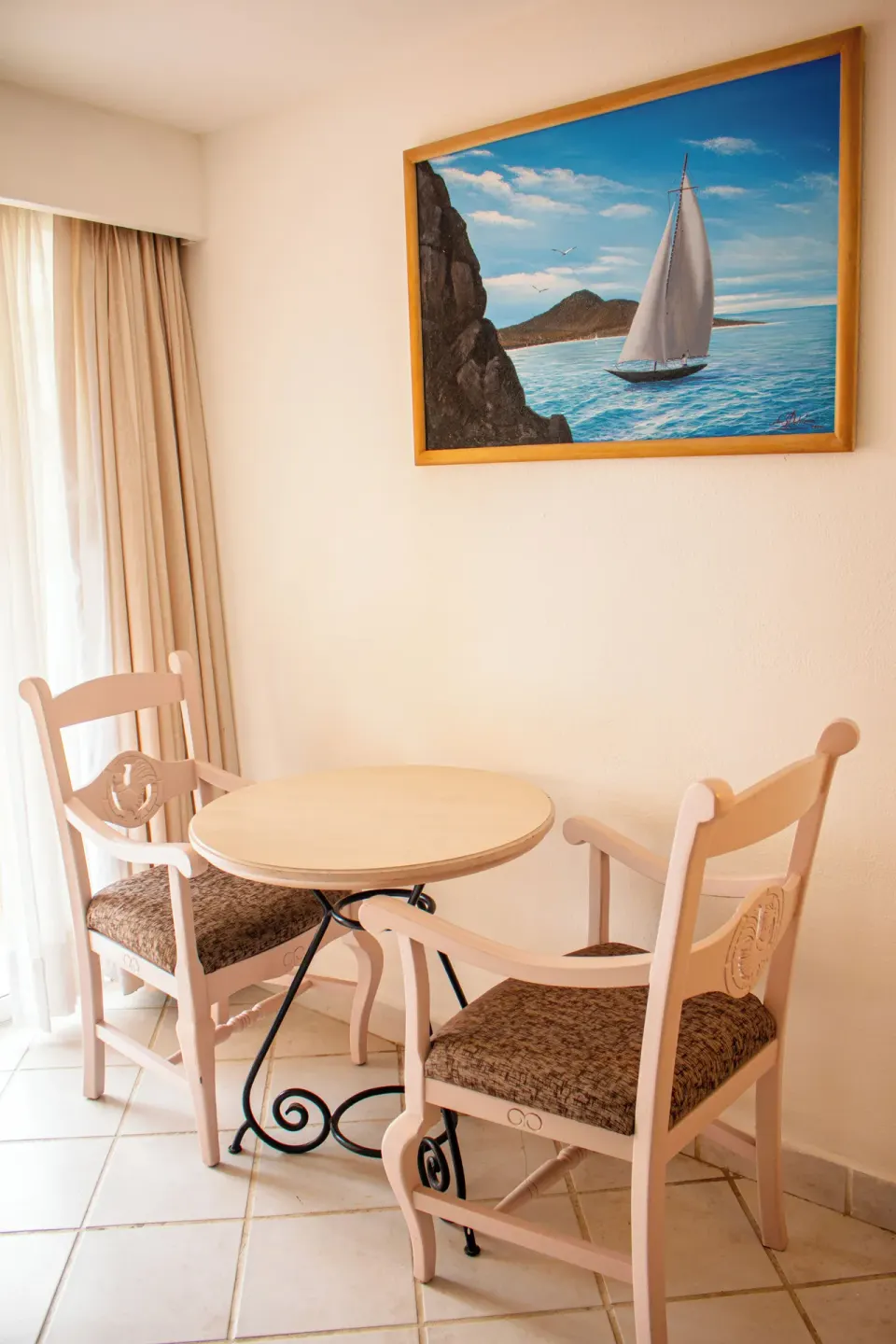 Small table with two chairs beneath coastal artwork in a room at Posada Real Los Cabos.