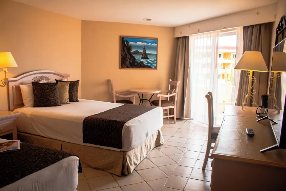 Standard room with two beds, desk, dining nook, and balcony light at Posada Real Los Cabos.